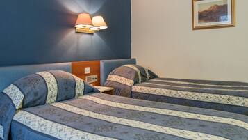 A hotel room with two beds, a nightstand, a wall-mounted lamp, and a framed picture on the wall.
