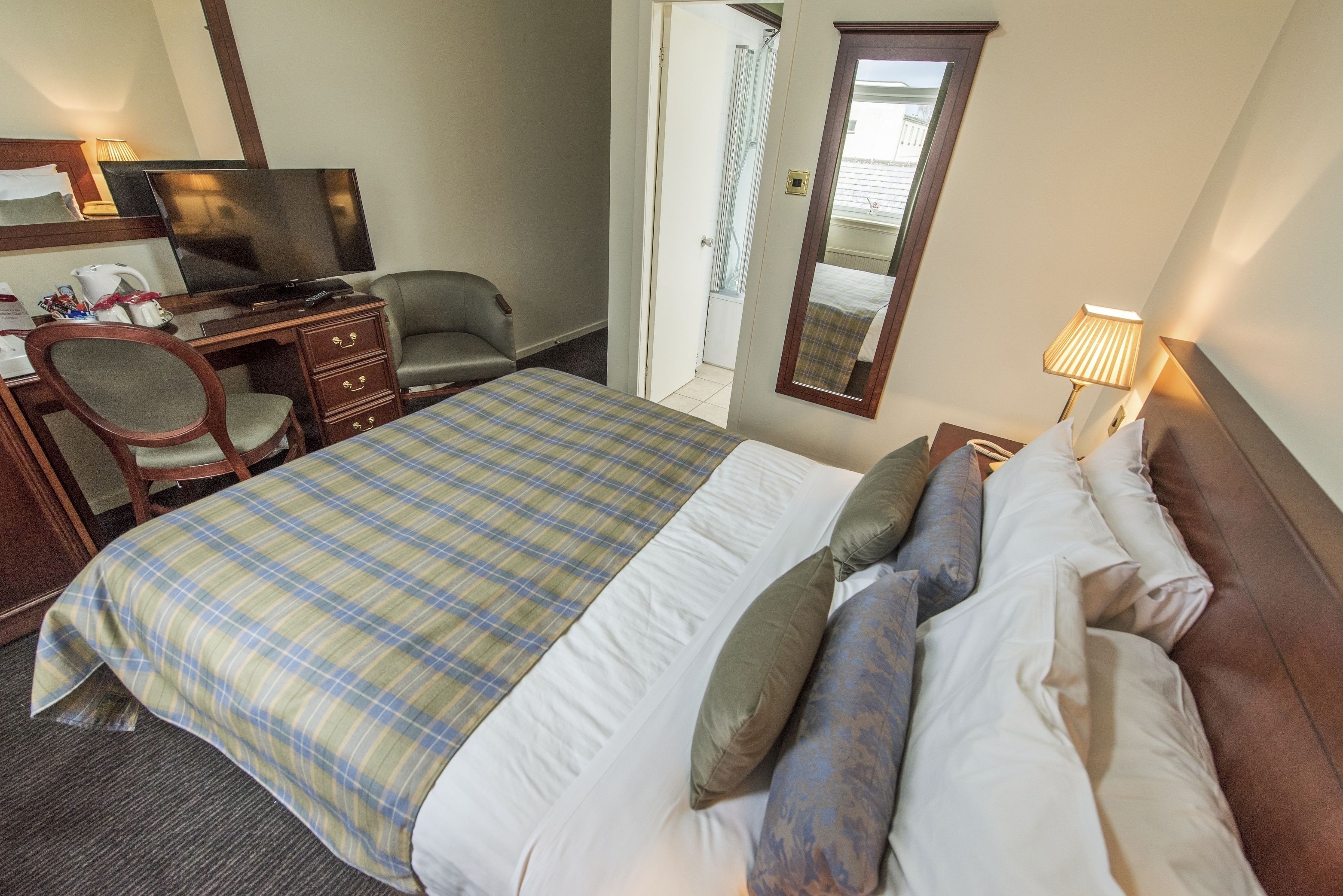 Una habitación de hotel con una cama, un escritorio con computadora, una silla, un televisor y un espejo.