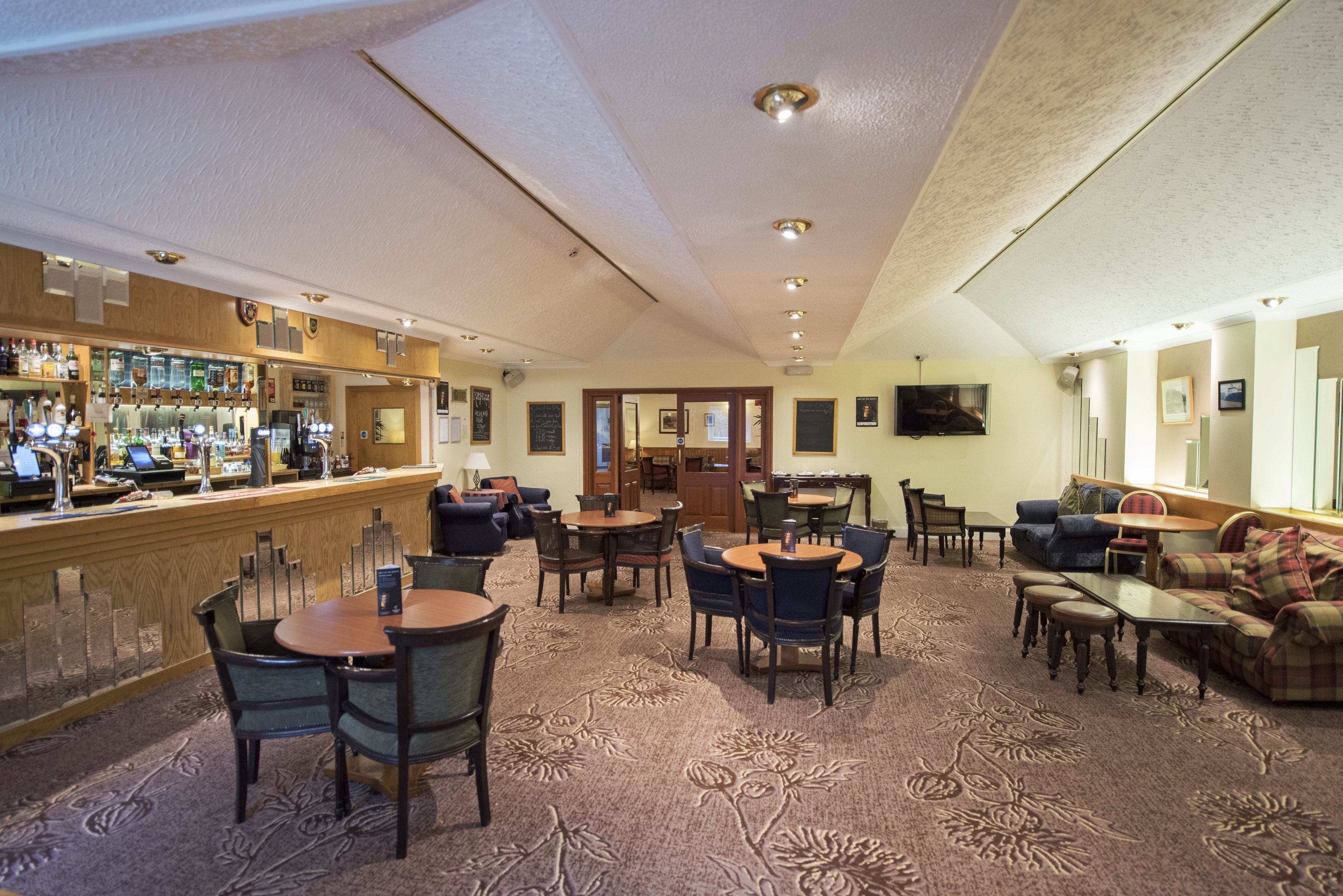 Un vestíbulo de hotel con zona de bar, disposición de asientos y suelo alfombrado.