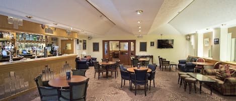 A hotel lobby with a bar area, seating arrangements, and a carpeted floor.