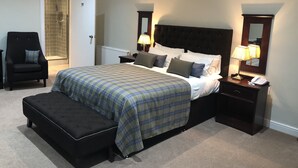 Une chambre à coucher avec un grand lit, un banc, une chaise, une table de chevet avec une lampe et une porte donnant sur une salle de bain.