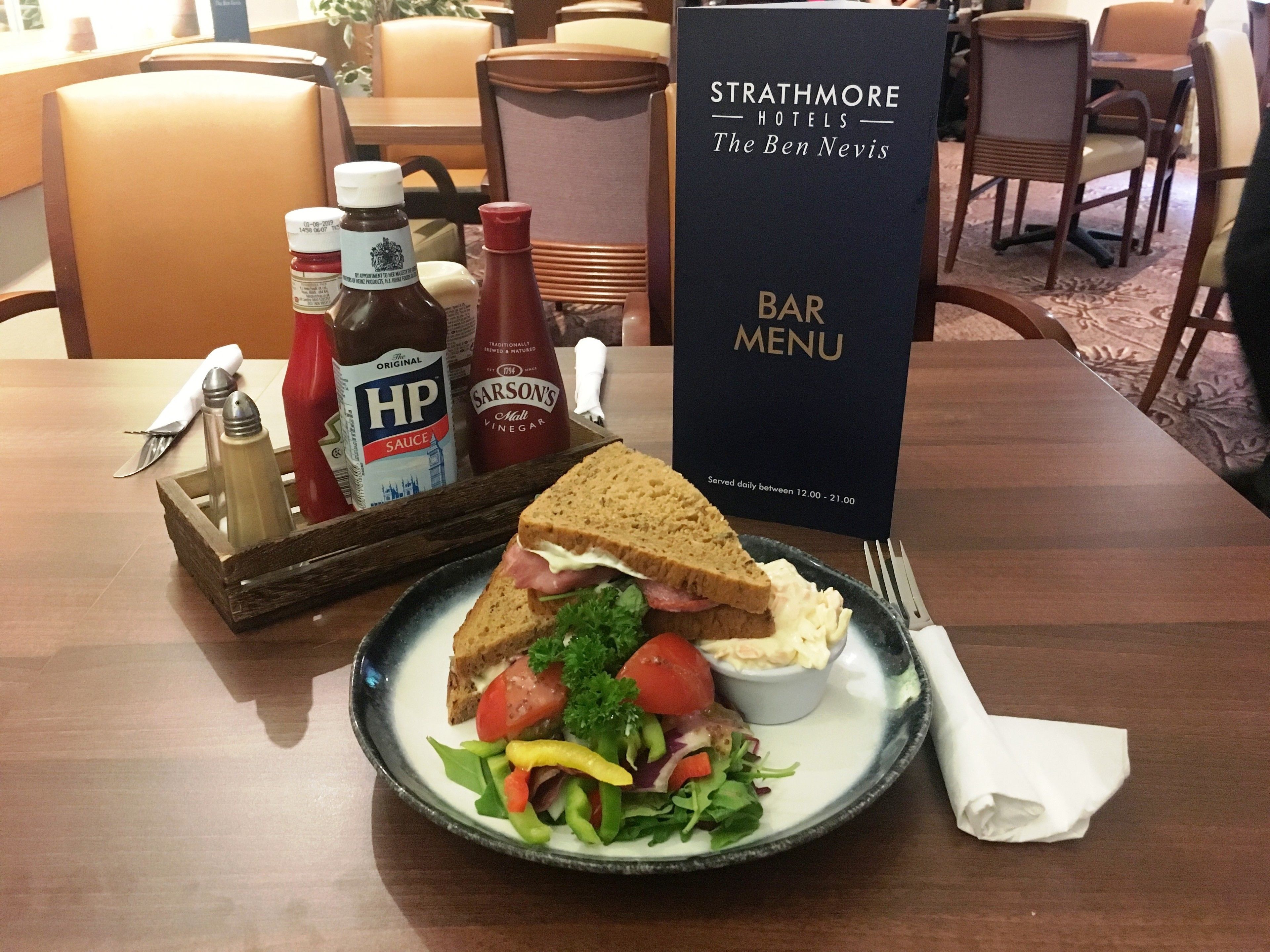 Une table à manger avec un sandwich, une salade, des condiments et un menu de bar.