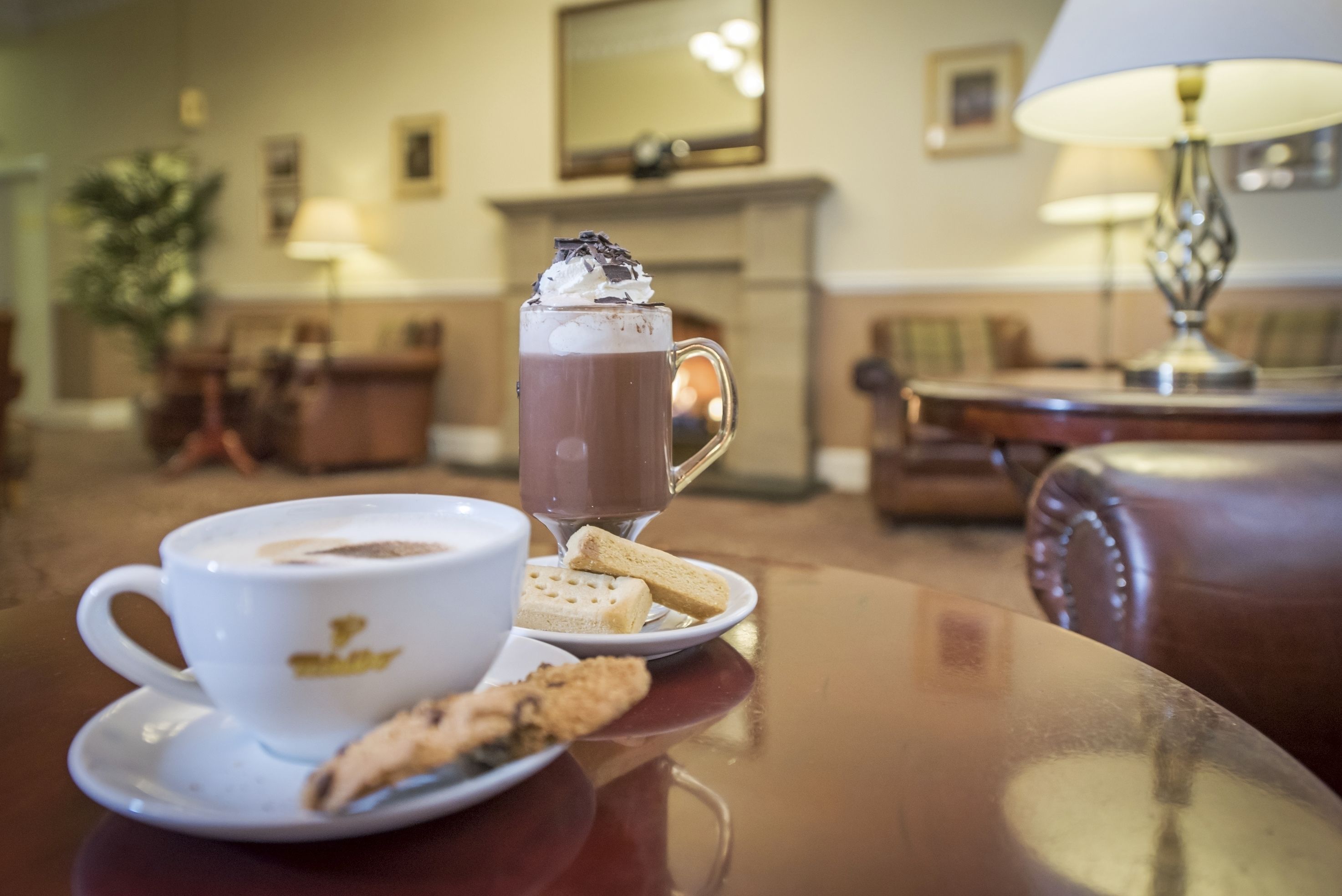 Una mesa con una taza de café, un vaso de chocolate caliente y galletas.
