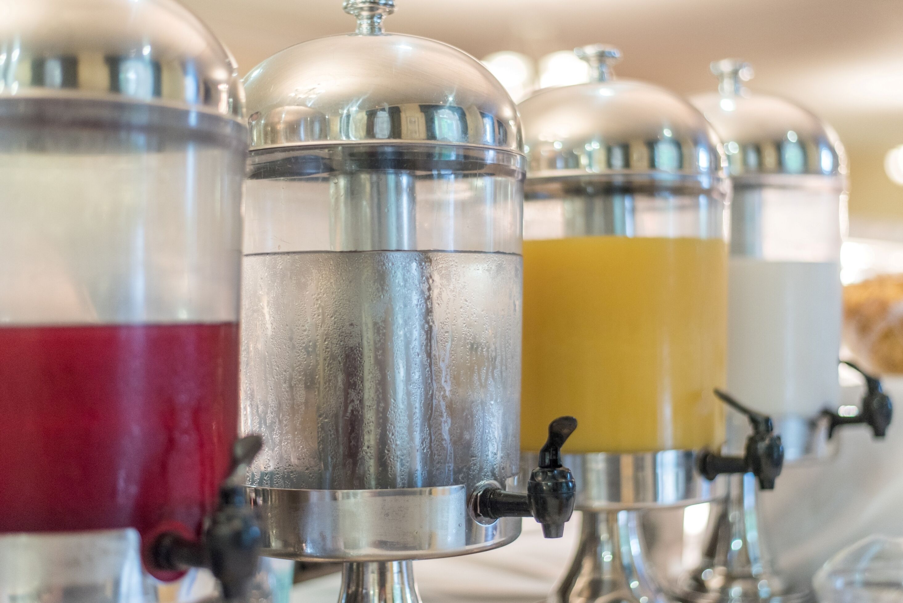 Una hilera de dispensadores de bebidas con tapas y grifos metálicos.