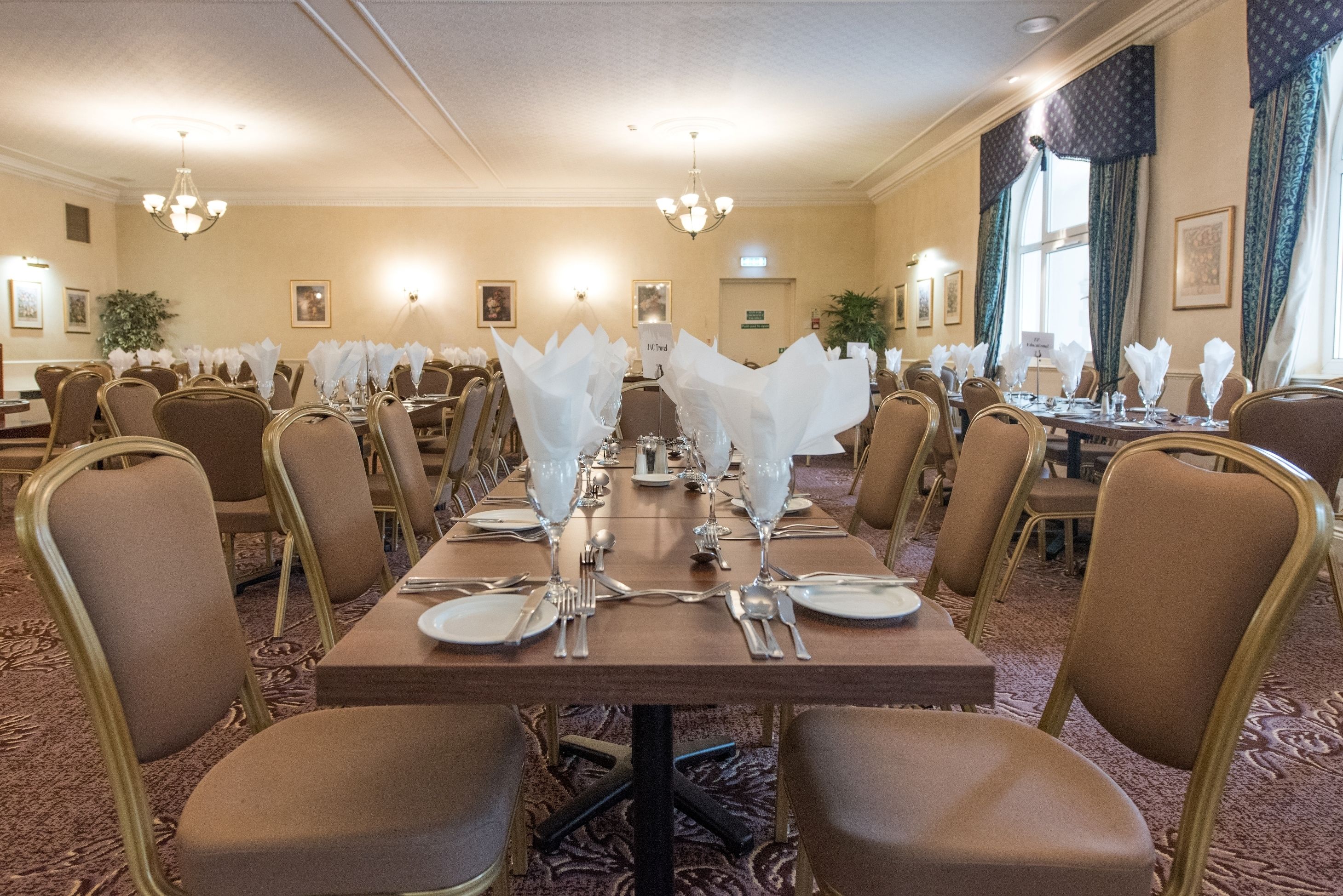 A banquet hall with multiple tables set for dining, each with white napkins, silverware, and glassware.