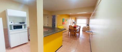 Une cuisine avec un îlot central jaune, des armoires blanches et un coin repas comprenant une table et des chaises.
