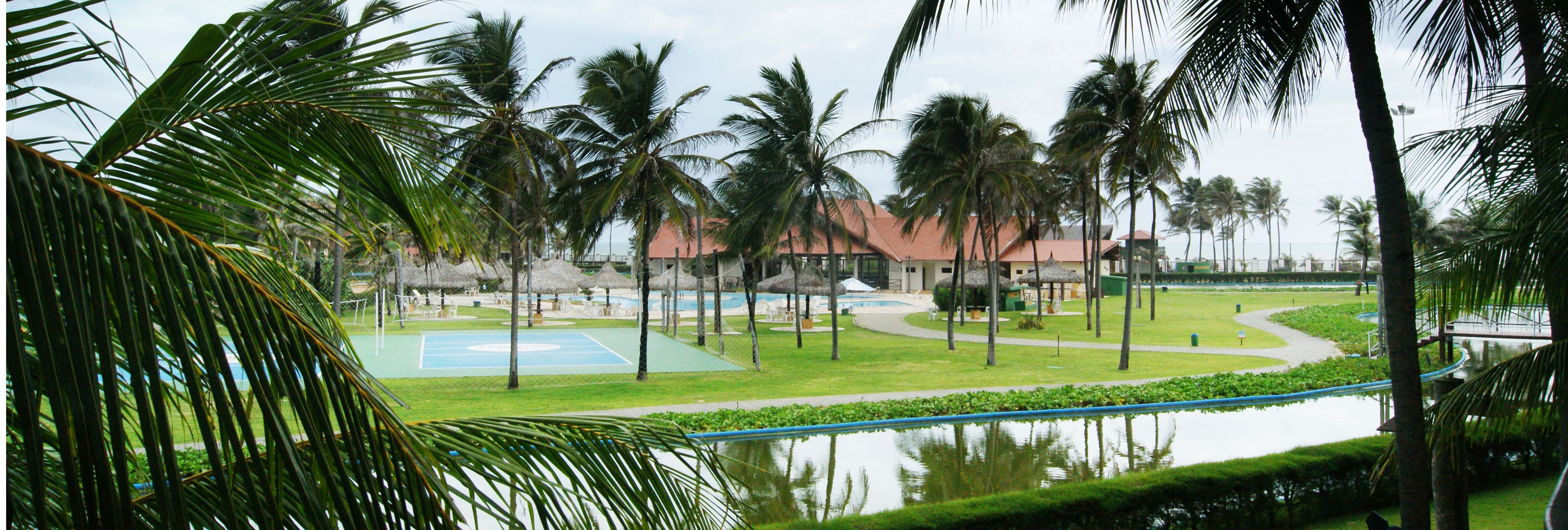 A tropical resort with a swimming pool, tennis court, and palm trees.