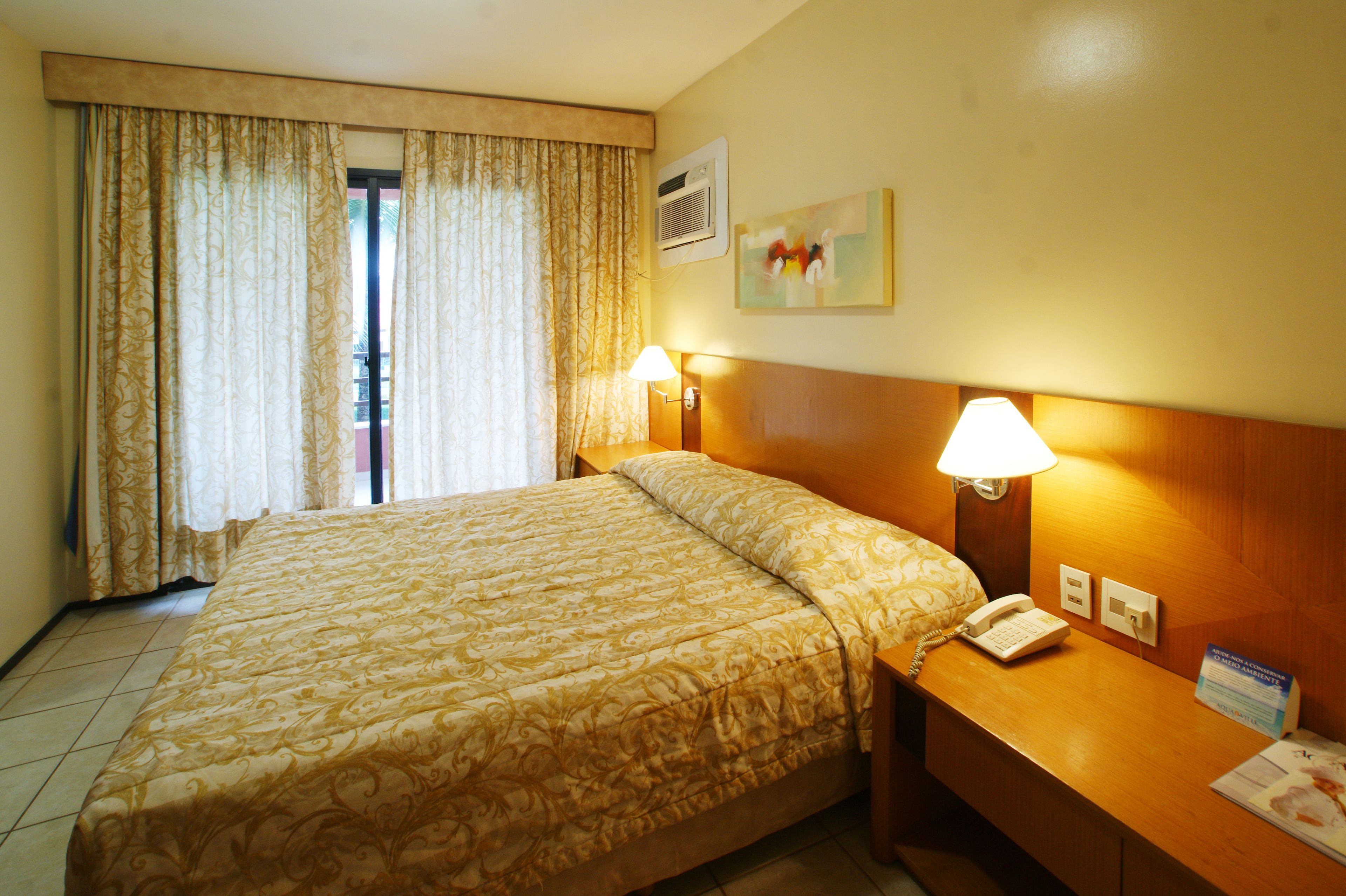 A hotel room with a large bed, two bedside lamps, a telephone, and a painting on the wall.