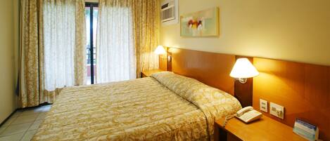 A hotel room with a large bed, two bedside lamps, a telephone, and a painting on the wall.