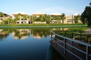 Un hotel frente al lago con muelle de madera, palmeras y aguas tranquilas.