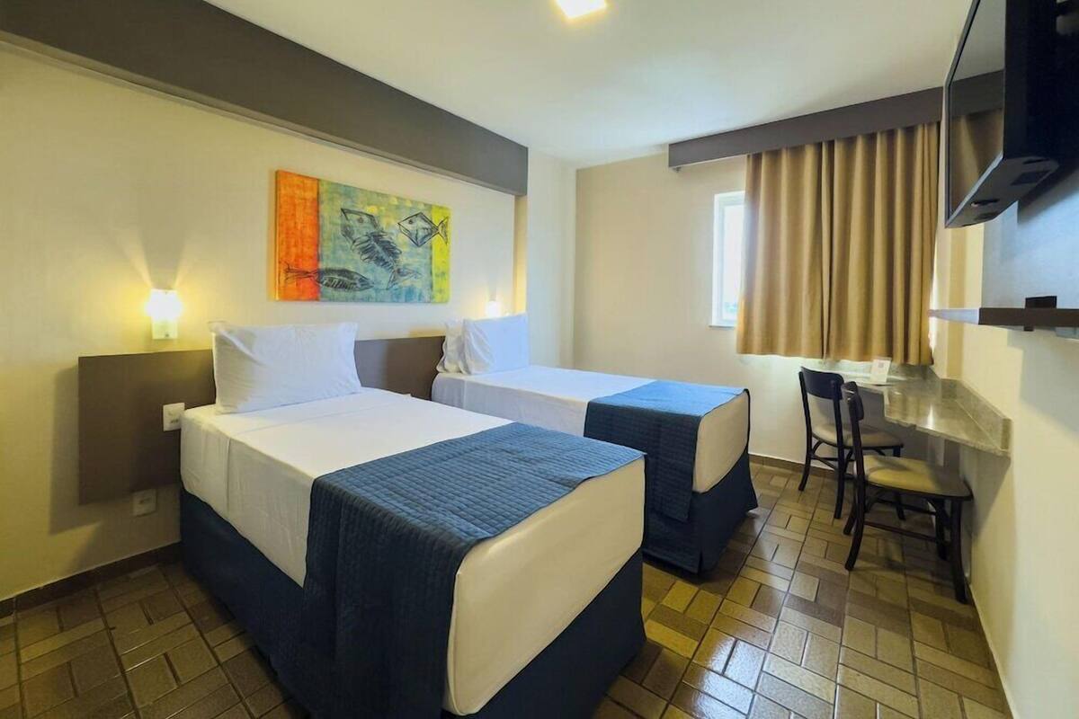 Een hotelkamer met twee bedden, een bureau, een stoel, een televisie en een schilderij aan de muur.