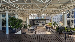 Un patio al aire libre con piso de madera, techo de estructura metálica y plantas en macetas.