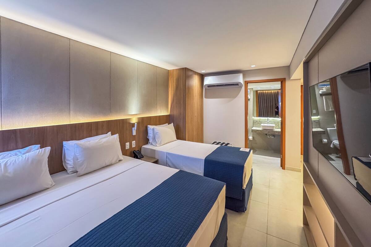 Een hotelkamer met twee bedden, een televisie en een badkamer zichtbaar door een geopende deur.