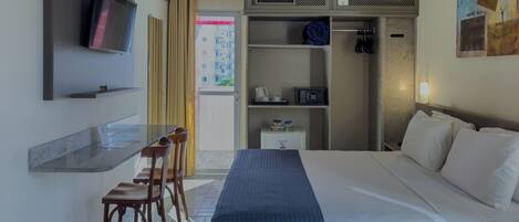 A hotel room with a bed, a desk with chairs, a television, a wardrobe, and a painting on the wall.