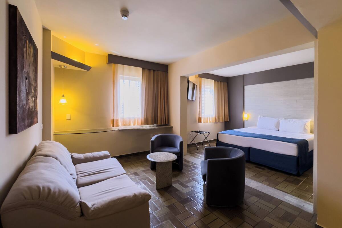 Een hotelkamer met een bed, een bank, een kleintje tafeltje en een stoel.