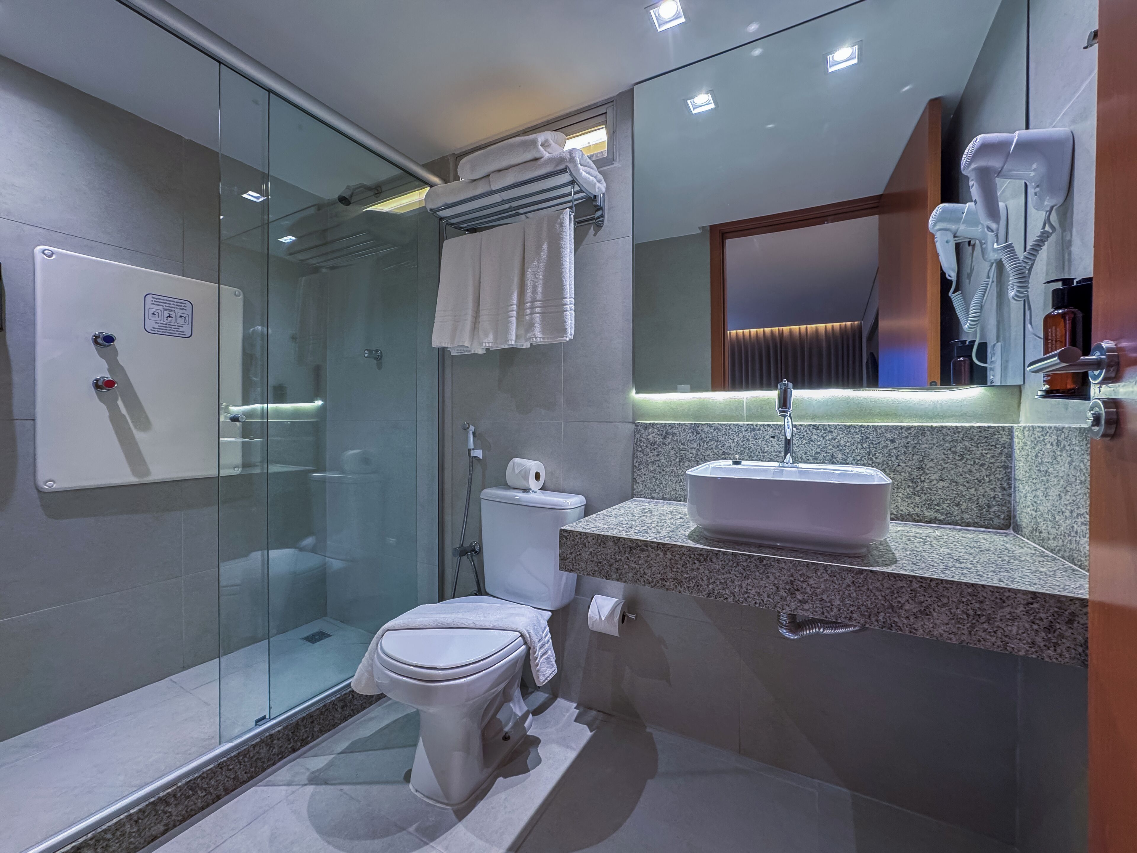 A modern bathroom with a glass shower enclosure, a toilet, a sink with a mirror above it, and a hairdryer mounted on the wall.