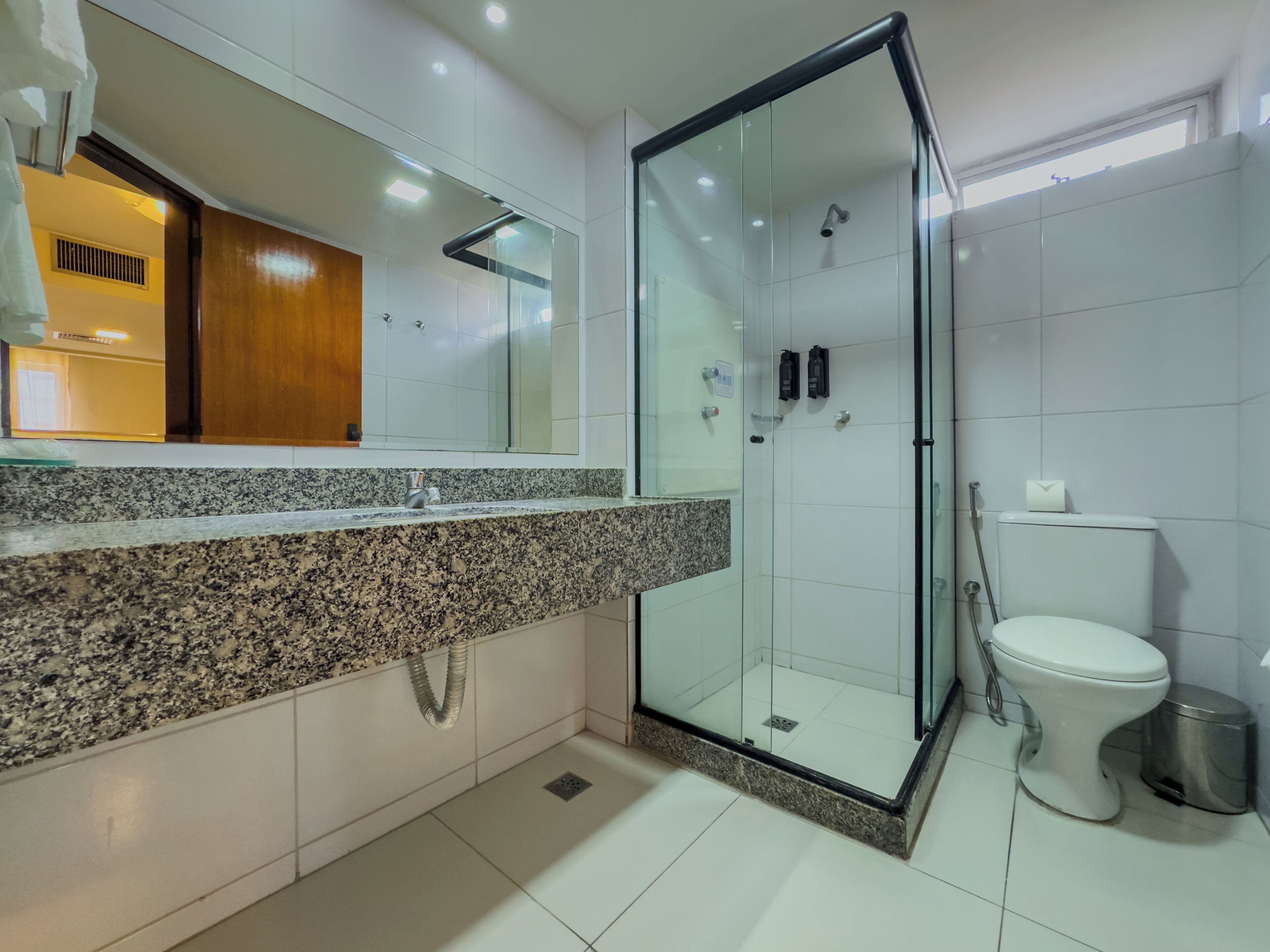 A modern bathroom with a granite countertop, a glass-enclosed shower, and a toilet.