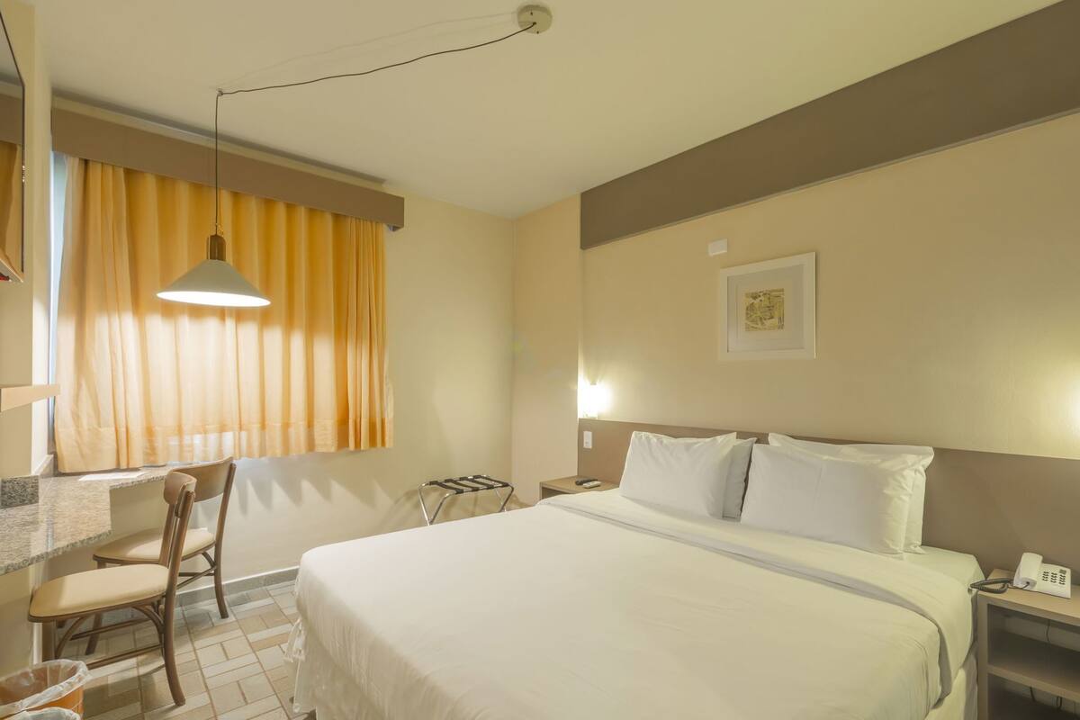 Een hotelkamer met een bed, een bureau met stoel, een telefoon en een wandlamp.