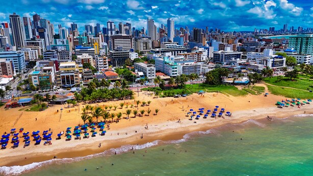 Un paisaje urbano costero con playa, palmeras y un horizonte urbano denso.