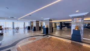 Un hall espacioso con suelo de mármol pulido, un mostrador de recepción y una estatua sobre un pedestal.