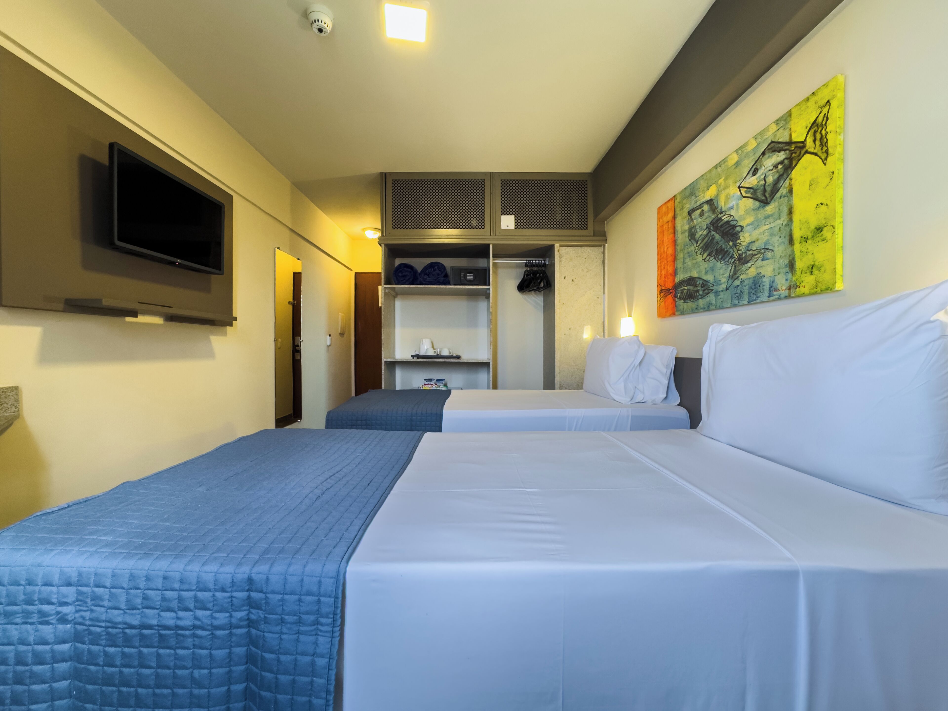 Habitación de hotel con dos camas, televisión, armario y un cuadro en la pared.