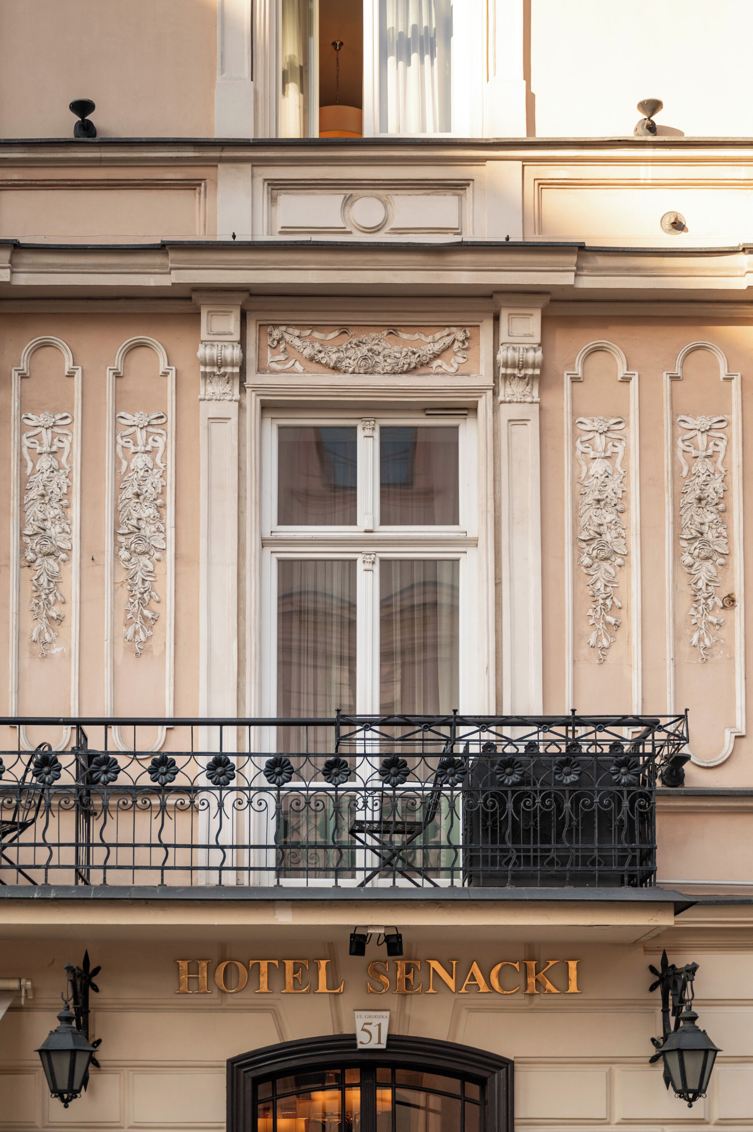 Un bâtiment doté de détails architecturaux raffinés, un balcon orné de balustrades en fer forgé et une enseigne indiquant « HÔTEL SENACKI ».