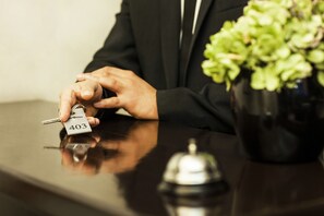 A hand holding a key with a tag labeled "403" next to a black desk with a silver bell and a potted plant.