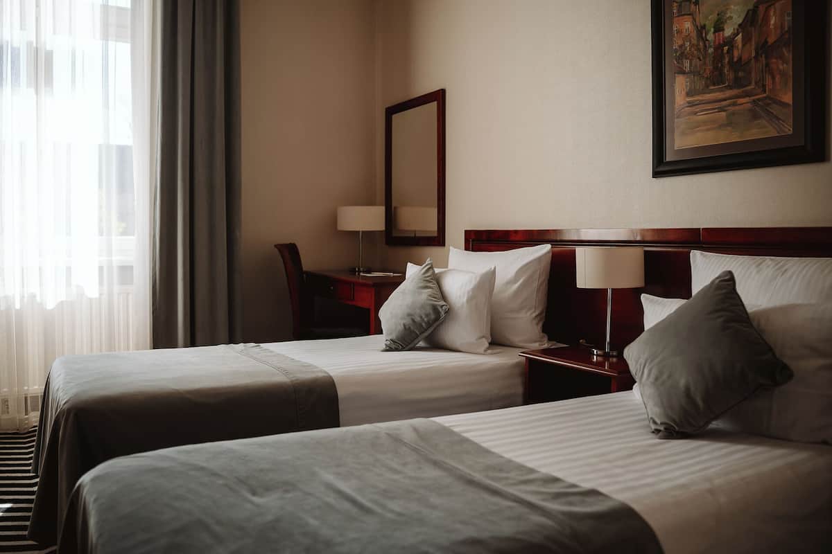 Ein Hotelzimmer mit zwei Betten, einem Schreibtisch, einem Stuhl, einer Lampe und einem Gemälde an der Wand.