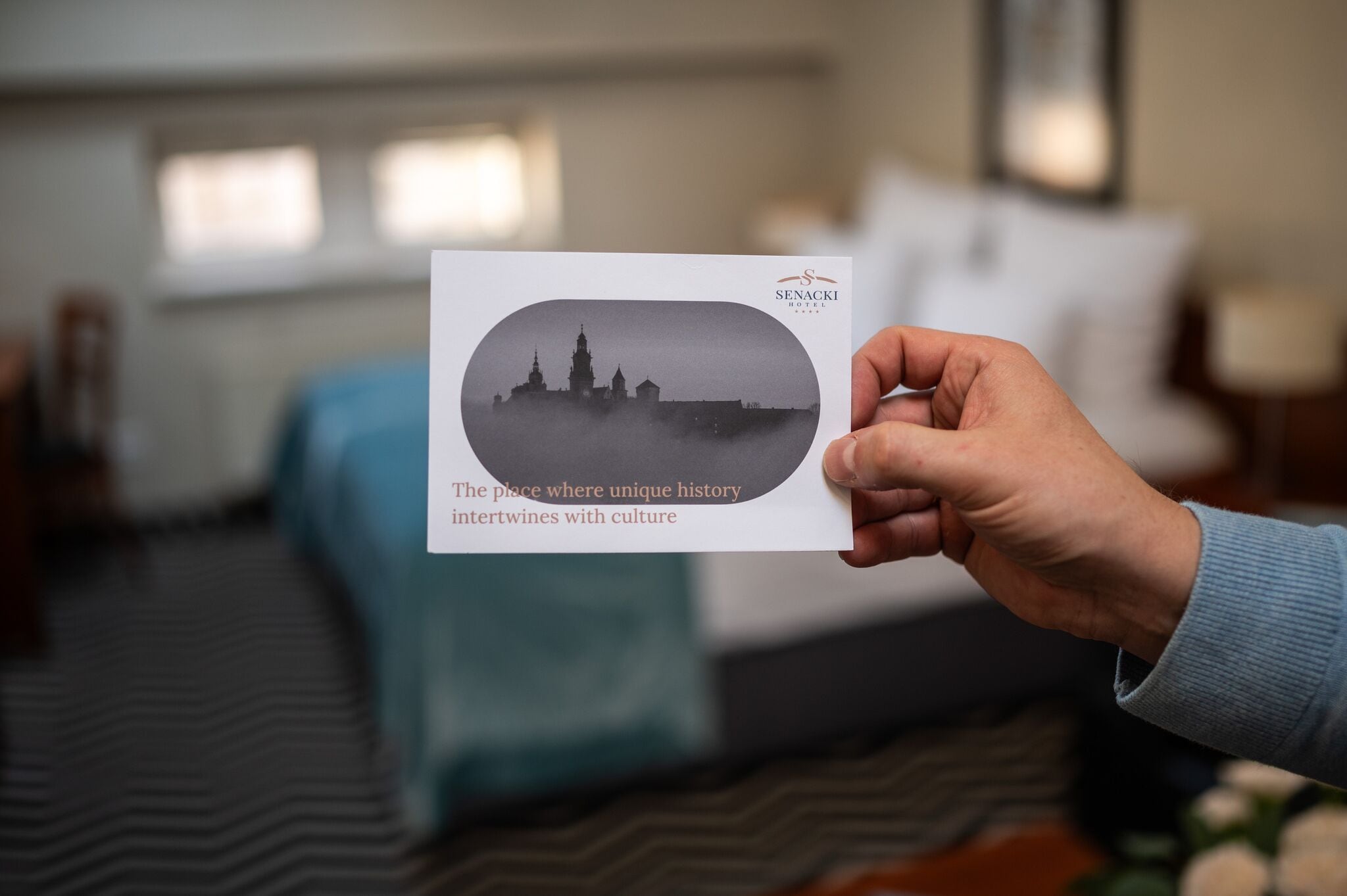 A hand holding a card with a black and white photo of a castle and text.