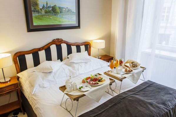 A hotel room with a neatly made bed, a breakfast tray with food and drinks, and a painting on the wall.