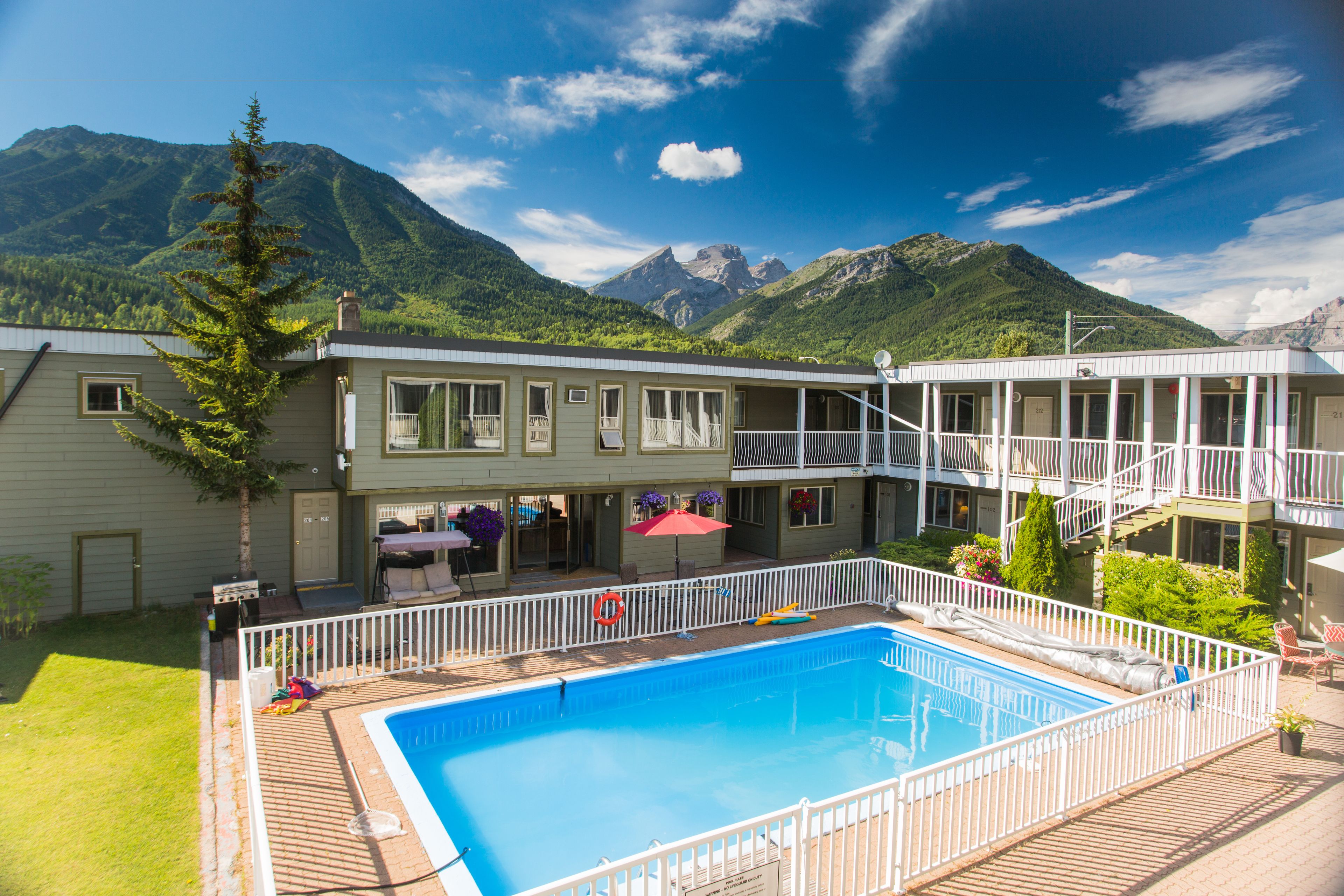 A two-story building with a swimming pool, a balcony, and a mountain backdrop.