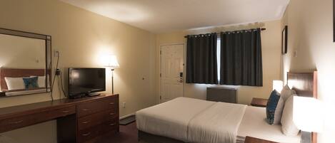 A hotel room with a bed, a desk, a television, a dresser, and a window with curtains.