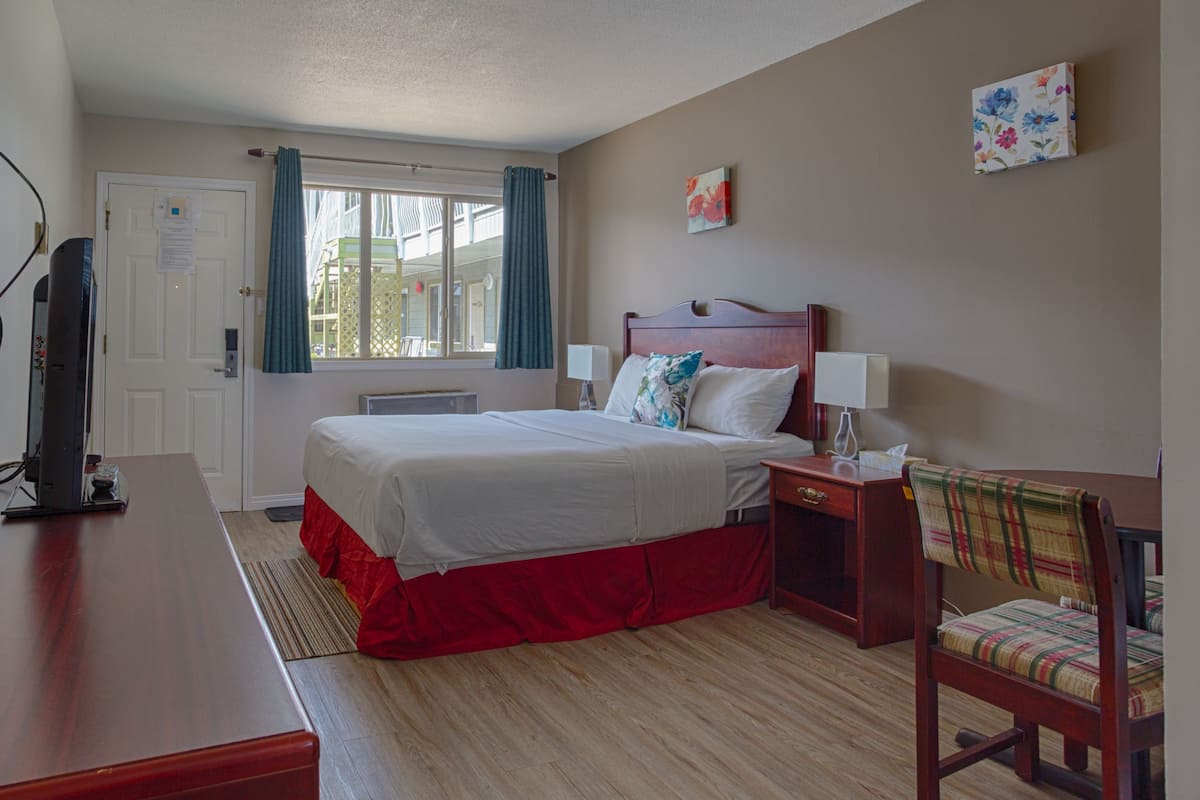 Habitación de hotel con cama, escritorio, silla, televisor y ventana con cortinas.