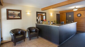 A reception area with a wooden reception desk, two leather chairs, a framed picture on the wall, and a clock on the wall. - Powder Mountain Lodge (Fernie)
