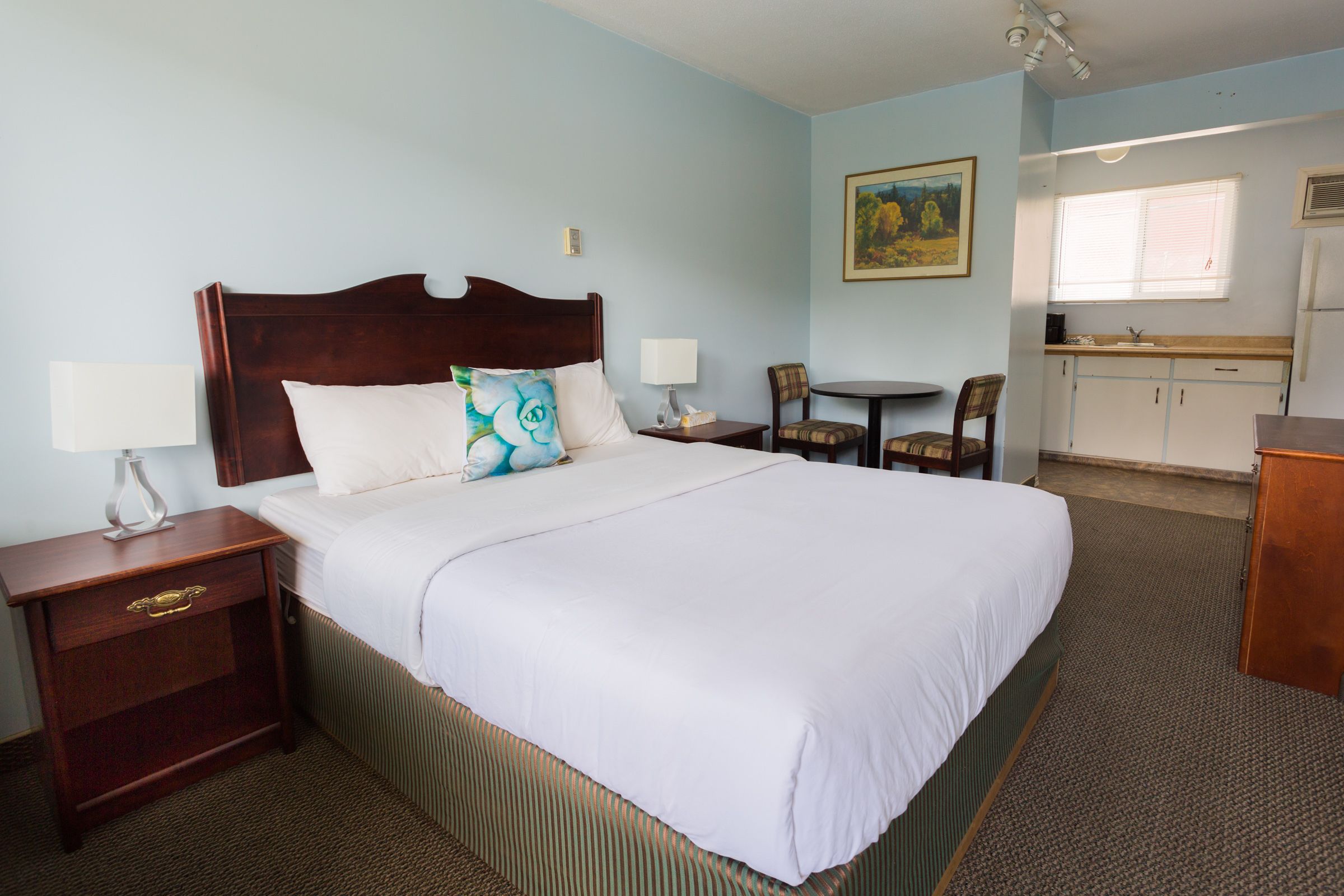 Habitación de hotel con una cama grande, mesitas de noche, una pequeña mesa de comedor y una kitchenette.