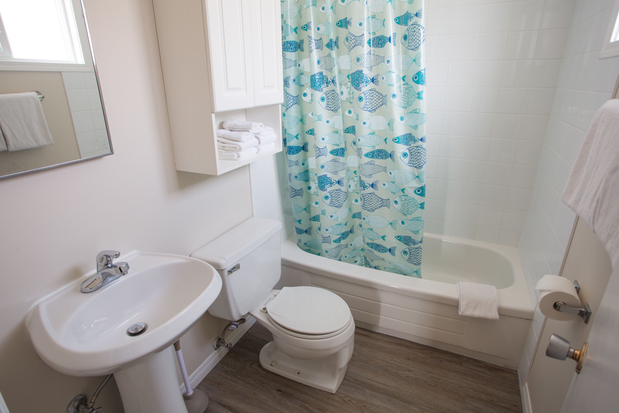 Un baño con lavabo, inodoro, bañera y cortina de ducha con estampado de peces.