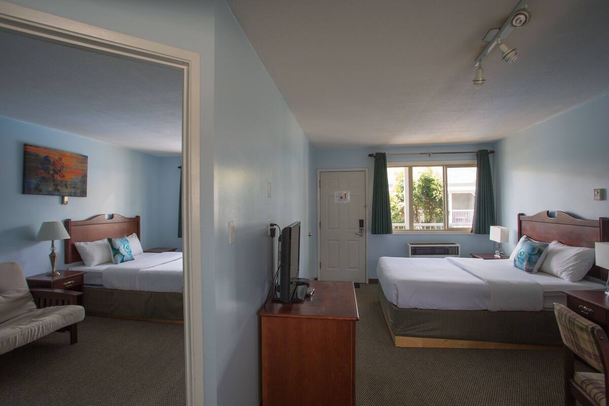 Habitación de hotel con dos camas, un escritorio, una silla, un televisor y una ventana con cortinas.