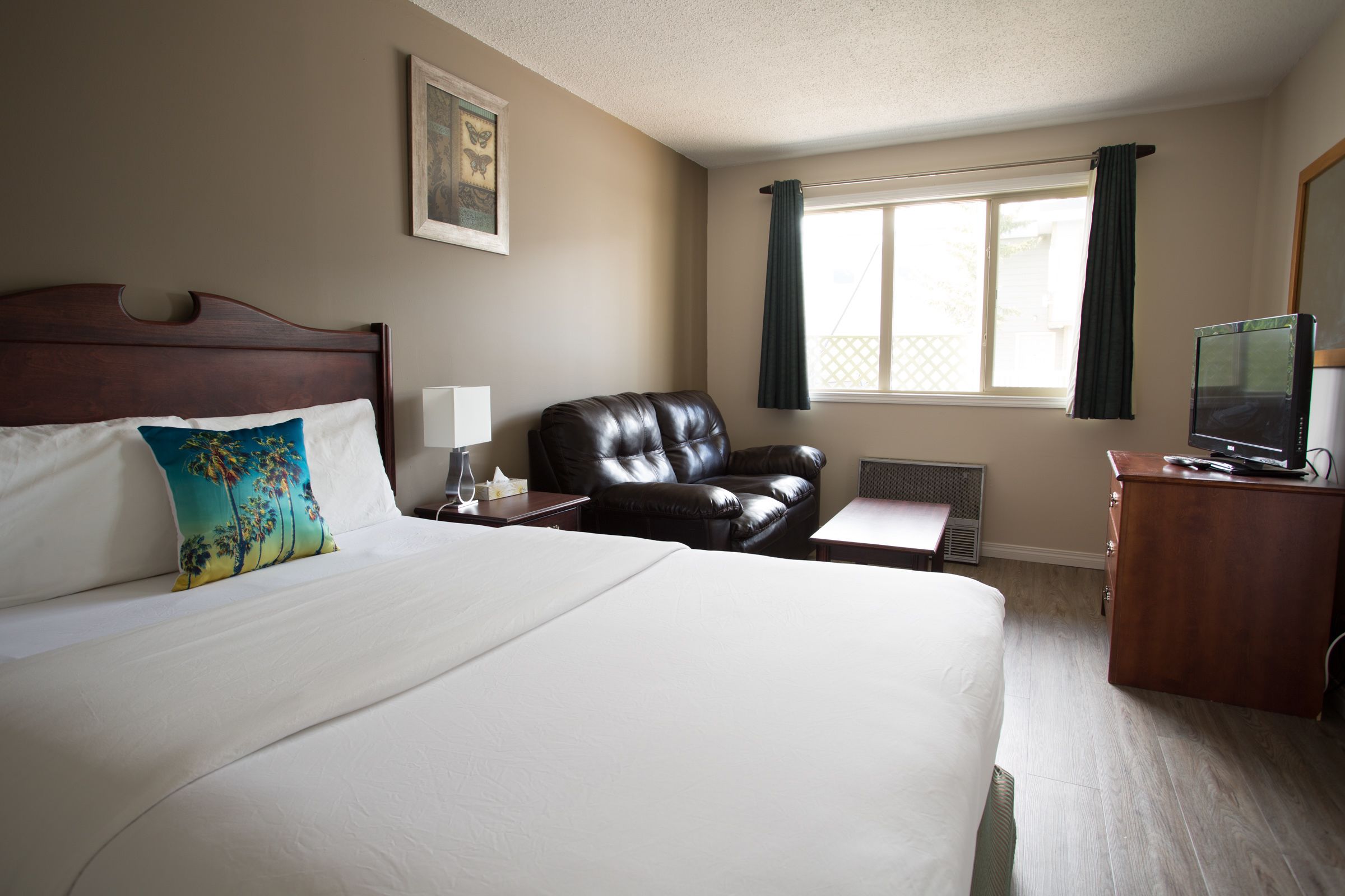 Habitación de hotel con una cama grande, un sillón de cuero, un escritorio con computadora y una ventana con cortinas.