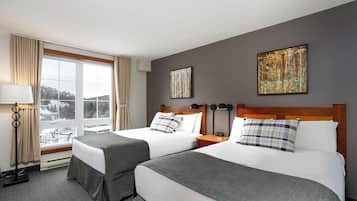 A hotel room with two beds, a large window, a lamp, and artwork on the wall.
