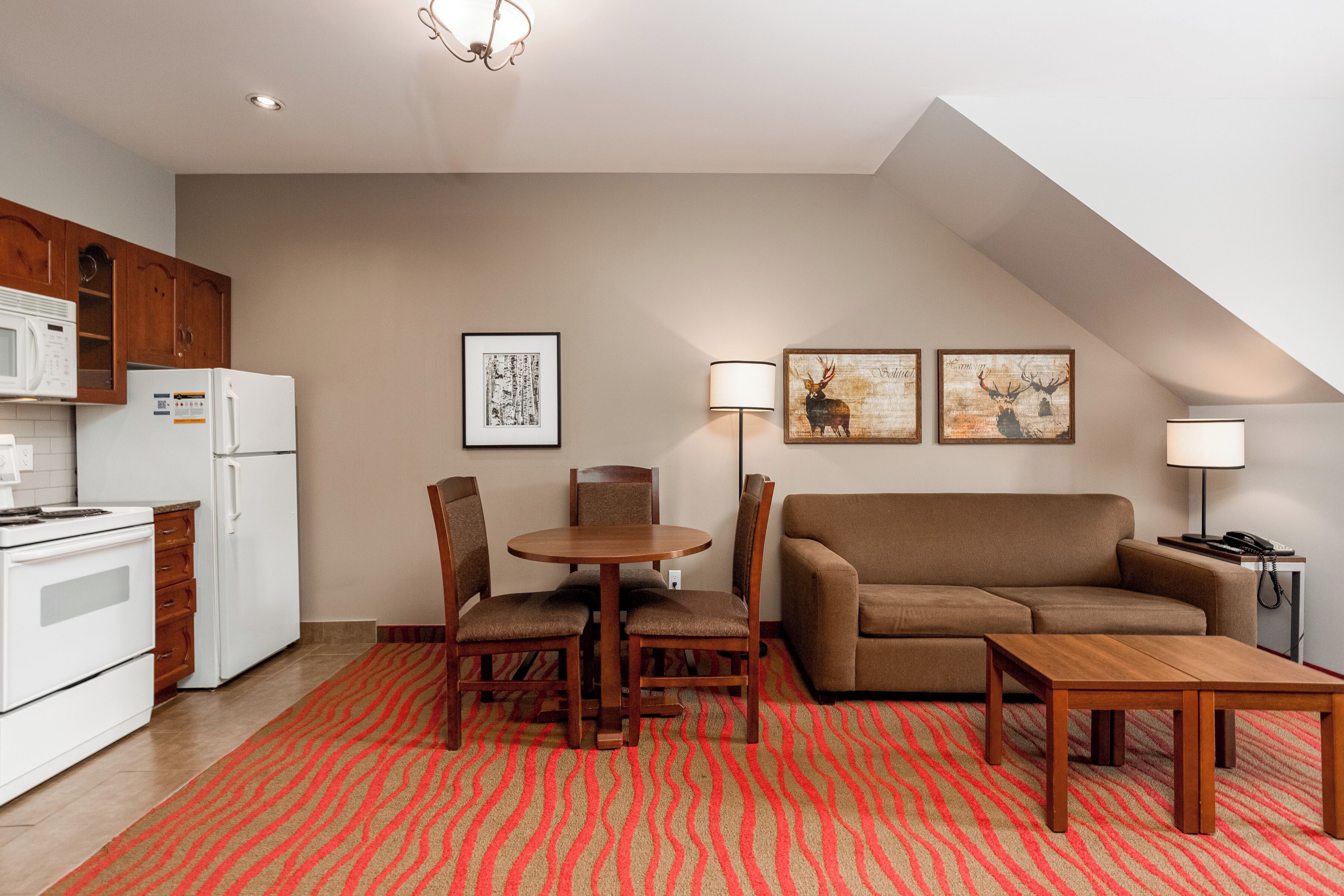 A compact living space with a kitchenette, a dining area with a table and chairs, a sofa, and two wall-mounted lamps.