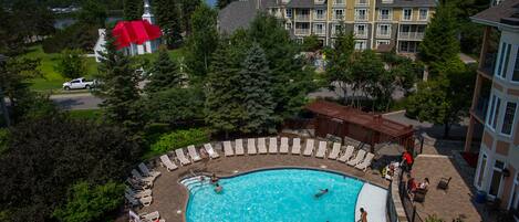A swimming pool surrounded by lounge chairs, a covered patio area, and a view of a church and residential buildings.
