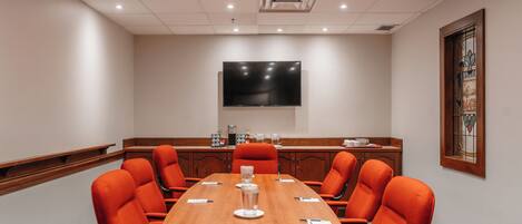 A conference room with a long table, orange chairs, a flat-screen TV on the wall, and a stained glass window.
