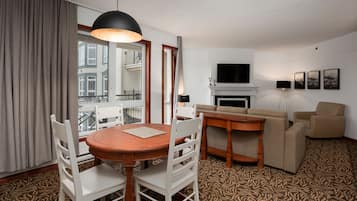 A hotel room with a dining table, chairs, a sofa, a TV, and a fireplace.