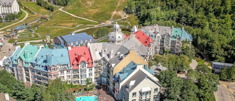 A multi-story hotel with a swimming pool, surrounded by lush greenery and a ski lift in the background.