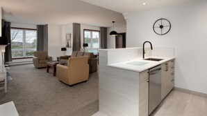 A modern living room with a sofa set, a dining table, and a kitchen area with a sink and cabinets. - Sommet des Neiges (Mont-Tremblant)