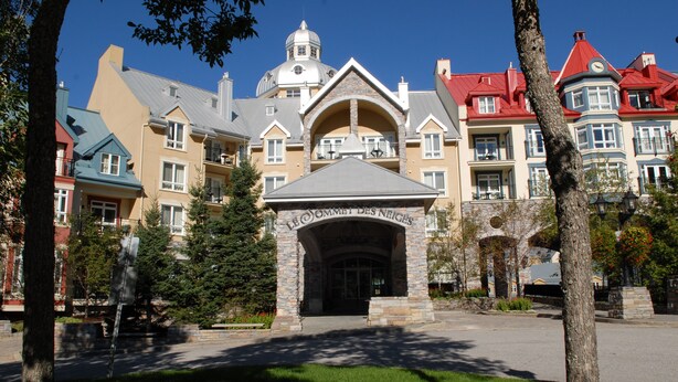 A hotel with a central entrance, multiple balconies, and a distinctive tower. - Sommet des Neiges (Mont-Tremblant)