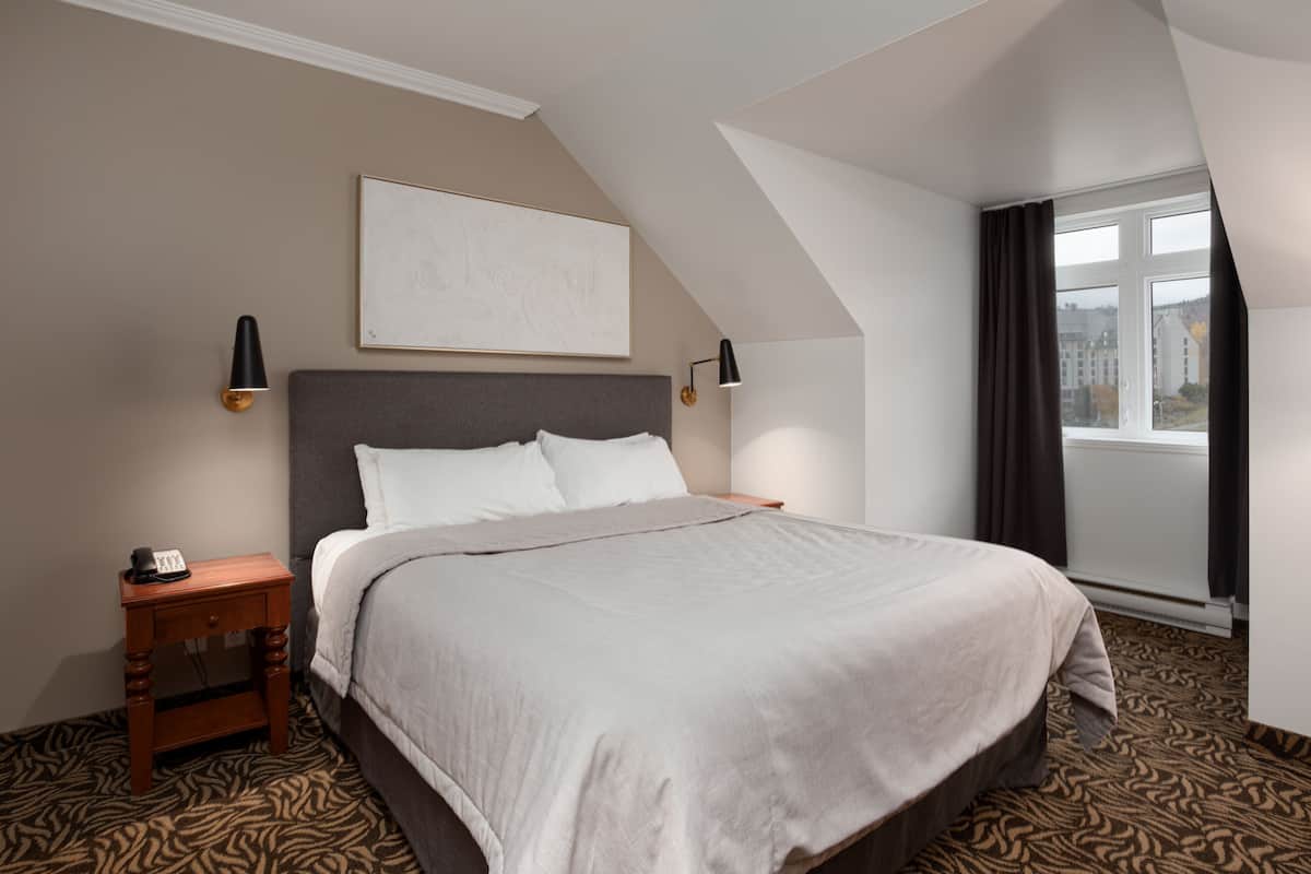 A hotel room with a bed, a nightstand, a lamp, a painting on the wall, and a window with curtains.