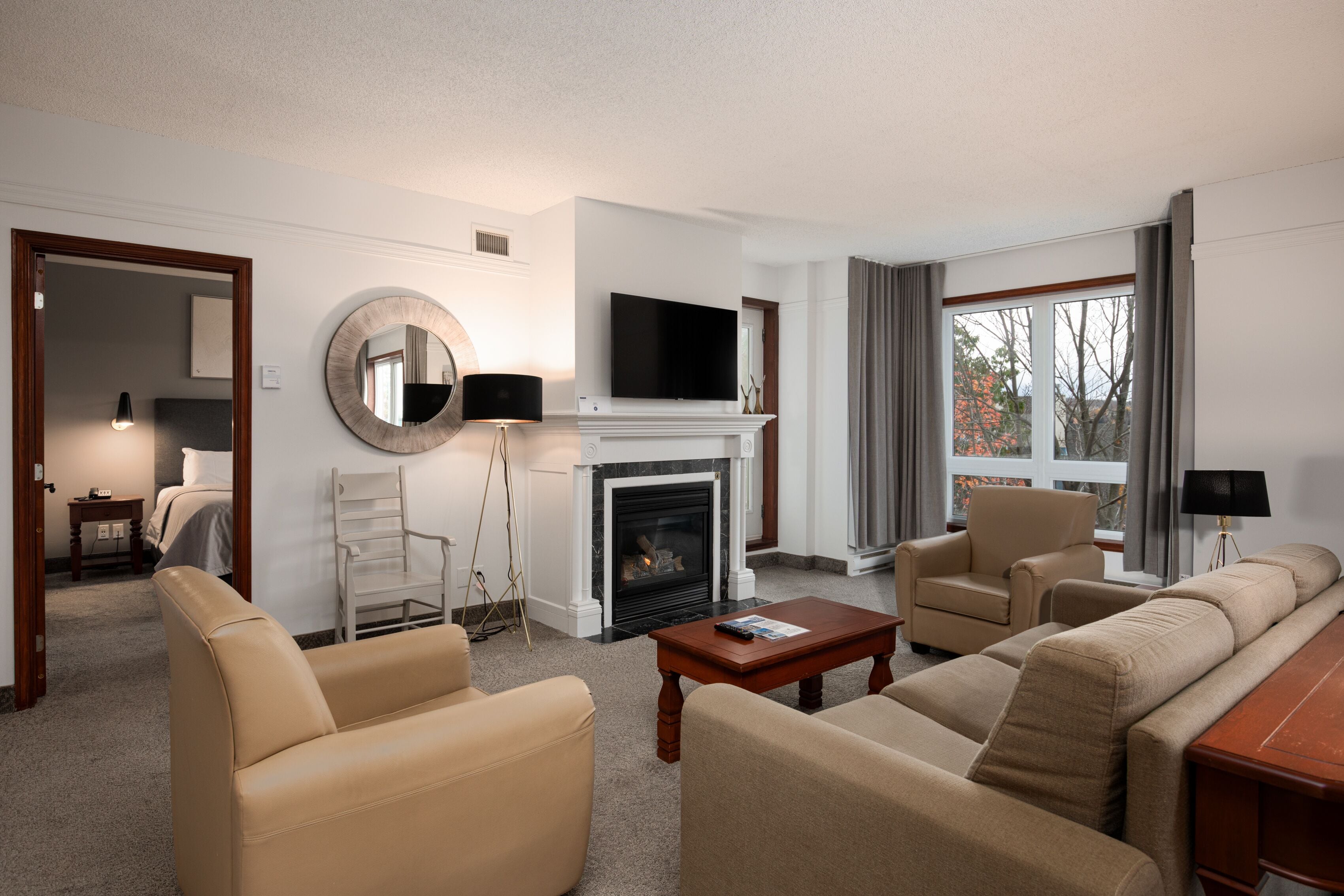 A modern hotel room with a fireplace, a flat-screen TV, a sofa, and a dining table.