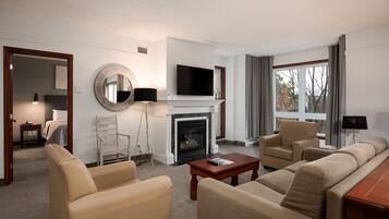 A modern hotel room with a fireplace, a flat-screen TV, a sofa, and a dining table.