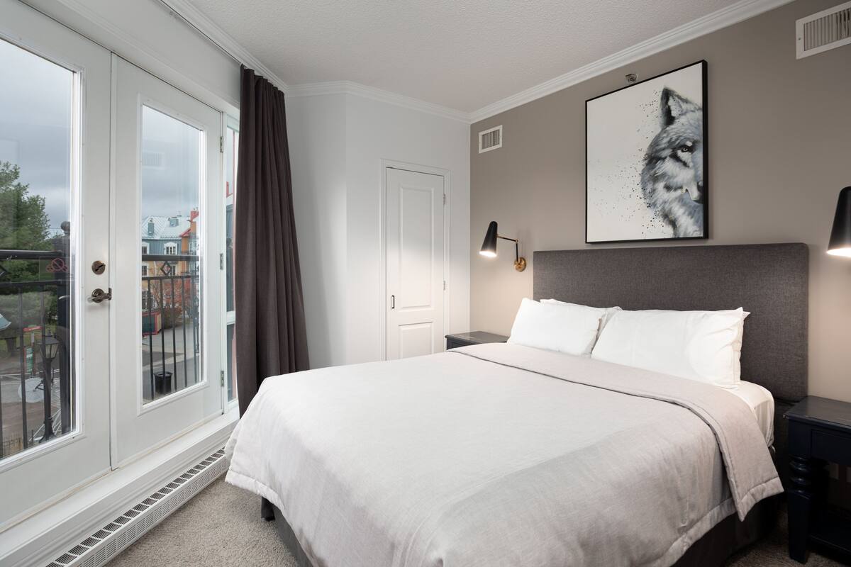A hotel room with a large bed, a window with curtains, a wall-mounted picture of a wolf, and a nightstand with a lamp.